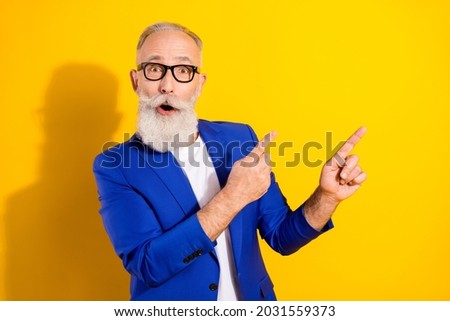 Photo portrait of senior man in blue suit amazed pointing fingers empty space isolated bright yellow color background