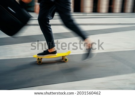 A blurry photo in motion. A businessman man goes to work. The manager rides a skateboard to the office. He holds a briefcase with documents in his hand.