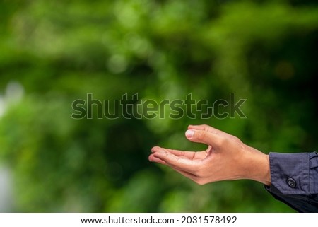 Man Hand over blur nature background, Hand holding object with fingers over blur nature background with empty space.