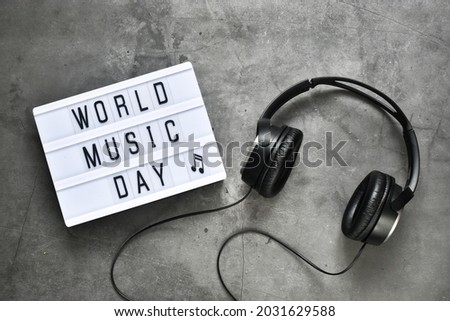 Stereo headphones and a light box with the inscription WORLD MUSIC DAY on a gray background. Flat lay. Copy space.