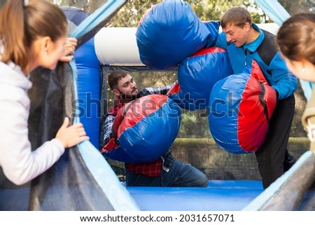 Happy male friends fighting by big stuffed boxing gloves at outdoor amusement playground