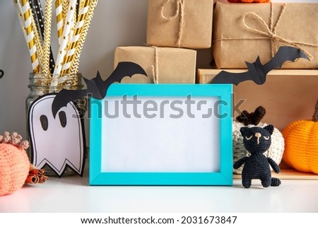 Halloween decor on a white background with a frame with empty space. Knitted pumpkins, witch hat, kerasin lamp, gifts in craft paper, blue frame