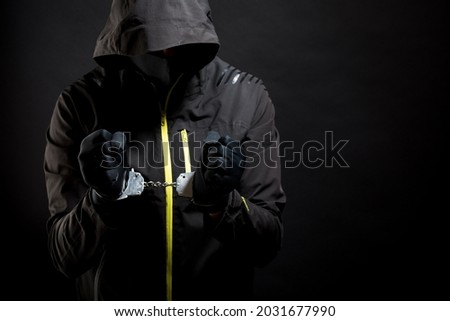 Unknown, indistinguishable thug or hucker in handcuffs and black clothes is arested. Concept: Crime because of crisis covid 19. isolated on black background Royalty-Free Stock Photo #2031677990