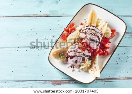 Gourmet banana split summer dessert with fresh strawberries and whipped cream topped with colorful sugar pearls and chocolate syrup in a top down view for menu advertising Royalty-Free Stock Photo #2031707405