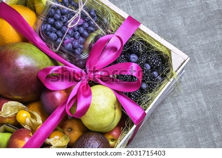 Juicy ripe fruits and berries are beautifully stacked in wooden box tied with pink ribbon. Dark background. Food delivery, gift fruit set. Concept of healthy eating, diet. Copy space. Selective focus. Royalty-Free Stock Photo #2031715403