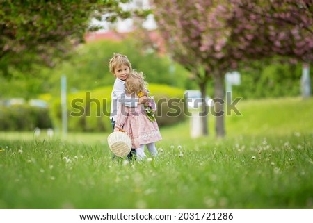 Beautiful children, toddler boy and girl, playing together in cherry blossom garden, running together and smiling with joy. Kids friendship, happy childhood