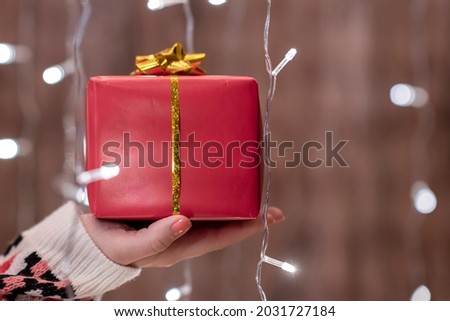 Woman hand holding out gift box through the glowing garland. Christmas