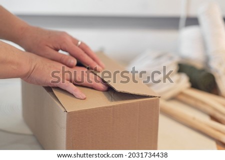 woman entrepreneur packs a handmade product in a cardboard box. delivery of goods for a small business. an elderly woman earns her hobby from home.