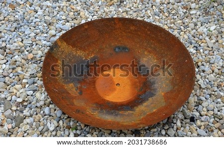rusty bowl with drain shaped like a big plate. The bowl stands on a gravel surface. The place serves as a fireplace neo barbecue place on the terrace in the garden park