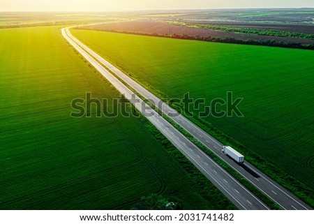 white truck driving on asphalt road along the green fields at sunset. seen from the air. Aerial view landscape. drone photography. cargo delivery Royalty-Free Stock Photo #2031741482
