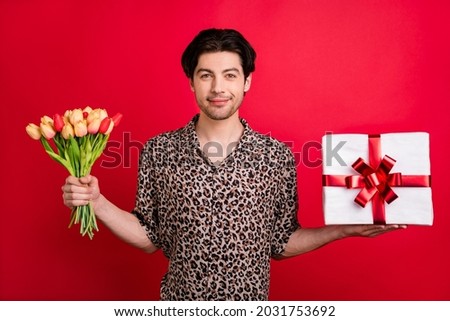 Photo of young smiling flirty coquettish boyfriend give valentine day present surprise box tulips isolated on red color background