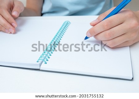 Female student hand holding a pen writing in a notebook, large poan, copy space. Business woman makes a note in a notebook. Back to school concept. Business concept