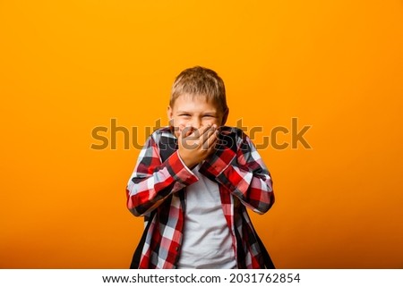 shocked little boy in red shirt covering his mouth with his hands on yellow background