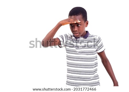 young boy in tee shirt standing on white background holding hand on forehead while looking away.