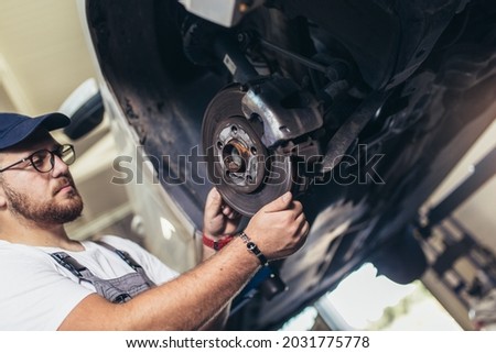 Professional near the car hanging on the lift at the service station make a diagnostics, repair the brakes