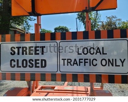 An orange and black sign blocking the road that reads "street closed".  This traffic sign also indicates that local traffic is the only one granted access to the street.