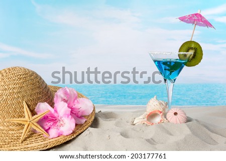 Blue cocktail on the beach with a sunhat and sea shells