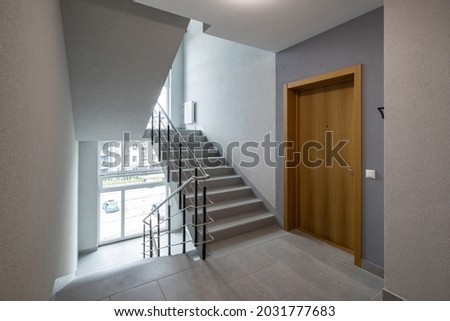 Modern interior of new entrance in residential building. Wooden door to apartment. Stairs and windows. Royalty-Free Stock Photo #2031777683