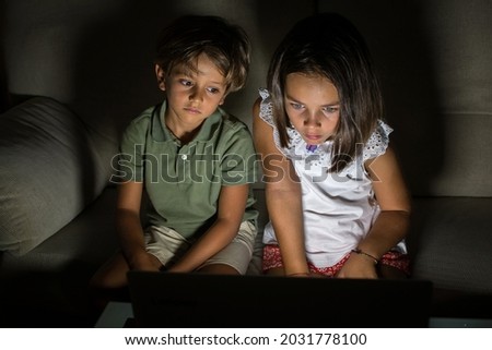 Children At Home. Stock Photo Of A Boy And A Girl At Home Watching A Movie Or Series On The Computer. They Have A Shocked Expression. They Are Dark And You Have The Light From The Laptop Screen
