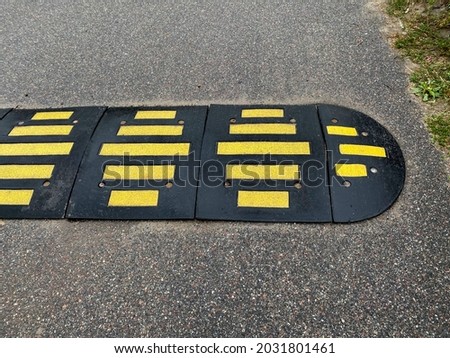 Artificial bumps in black rubber with contrasting yellow stripes. Compulsory braking device on a country road. Sleeping policeman (speed bump) on the road