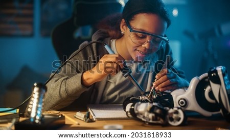 Young Teenage Multiethnic Schoolgirl is Studying Electronics and Soldering Wires and Circuit Boards in Her Science Hobby Robotics Project. Girl is Working on a Robot in Her Room. Education Concept. Royalty-Free Stock Photo #2031818933