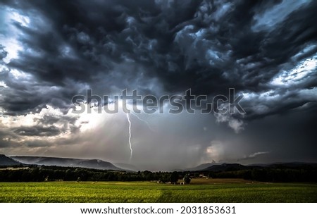 Lightning strike through the storm clouds over the field. Thunder clouds in evening sky
