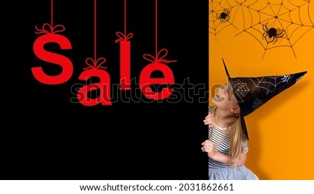 A little girl dressed as a witch peers out from behind a black wall that says SALE. Banner and copy space for your design.