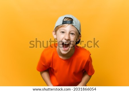 a computer gamer boy on a yellow background shows emotions. a child in a cap and an orange T-shirt is playing a game station