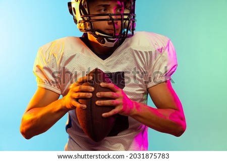 Energy. Close-up portrait of male american football player playing, training isolated on blue background in neon light. Concept of sport, movement, achievements. Copy space for ad