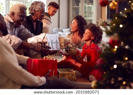 Multi-Generation Family Exchanging And Opening Gifts Around Christmas Tree At Home