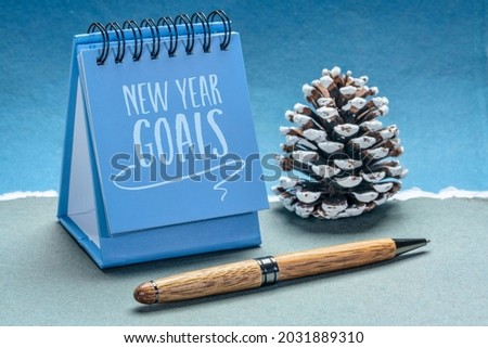 New Year goals - handwriting in a small desktop calendar with a frosty pice cone against abstract paper landscape, goal setting and resolutions concept