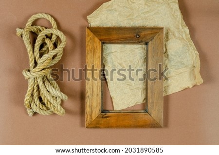 An empty photo frame and a roll of rope on a brown background. A wooden picture frame. Natural cord. Crumpled piece of wrapping paper. Top view.