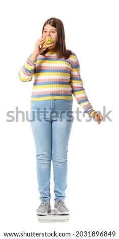 Overweight girl with burger standing on measuring scales against white background