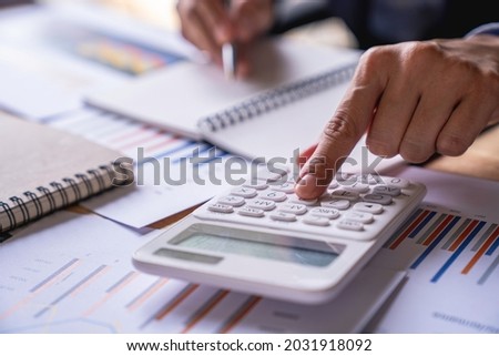 Accountant or banker working process, a Businesswoman using a calculator to calculate the numbers of statistic business profits growth rate on documents graph data, his desk in an office.