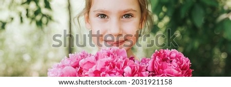 portrait of a happy cute little caucasian seven year old kid girl, holds in hands a bouquet of pink peony flowers in full bloom on the green background of nature. banner
