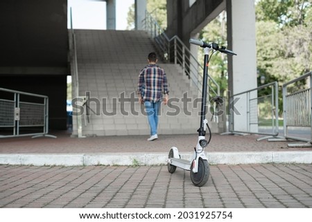 The man parks the electric scooter outside the mall and leaves. View from the back without a face. Ecological technological lifestyle. Electronic mobility. Copy space.