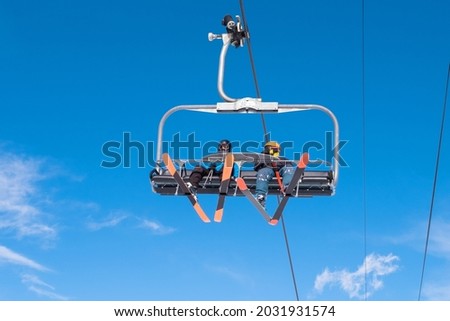 People riding ski chairlift. View from below. Group of people traveling on ski lift on top of mount for enjoing ski and snowboard. Winter sport, travel and vacation concept.  Royalty-Free Stock Photo #2031931574