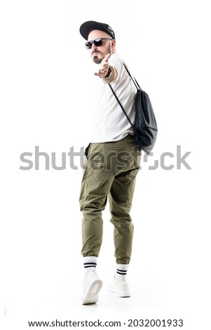 Cool nerdy stylish man walking away beckoning and inviting to join with hand gesture. Full length portrait isolated on white background