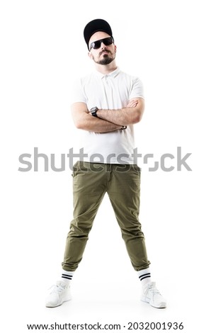Cocky confident attitude stylish young man posing with crossed arms wearing cap and sunglasses. Full length portrait isolated on white background