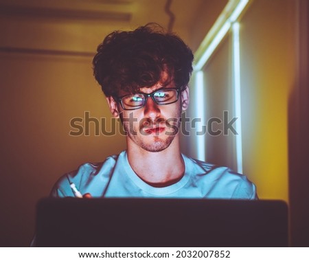 Caucasian Male with glasses worker is working on bright screen laptop computer at night with serious looking.