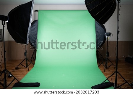 Front view of a green screen cloth backdrop with four photography LED softbox lights on tripods illuminate to the backdrop, get ready for take a shoot, making a video or broadcast TV in the studio.