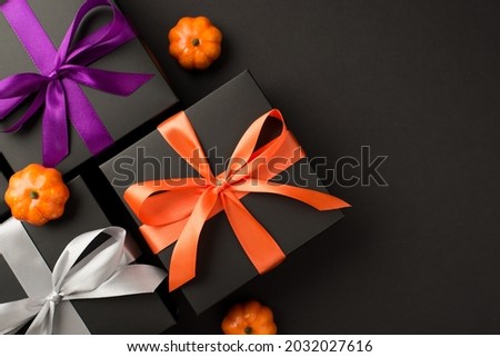 Top view photo of three black gift boxes with violet orange and white ribbon bows and small pumpkins on isolated black background with copyspace