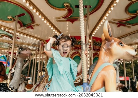 funny little girl in a blue dress rides on an amusement park ride