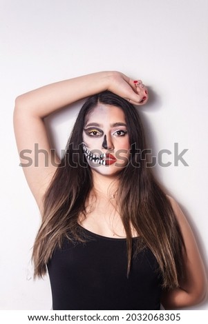 Portrait of a girl with Halloween skull makeup raising an arm above her head on white background.
