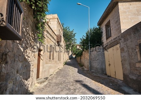 Narrow street in Urgup traditional houses made of limestone and cobblestone street and trees Royalty-Free Stock Photo #2032069550