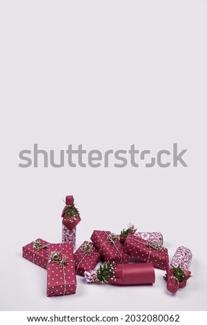 Decorating gifts in beautiful paper. Festive packaging of boxes and bottles with gypsophila flowers. Greeting card with boxes in burgundy color on gray background with floral arrangement for holidays.