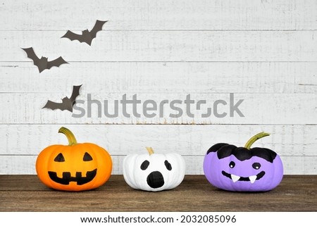 Painted Halloween pumpkins on a wood shelf against a rustic white wood background with bats. Jack o Lantern, ghost and vampire.