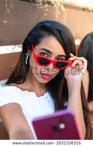 Beautiful latin girl taking a selfie. Hispanic woman taking a picture for her social media. Woman with red glasses looking at camera. Brunette woman in a summer day.