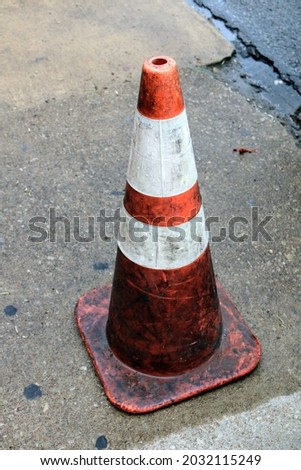 Closeup picture of a dirty construction cone sitting on concrete with faded line markings in sight