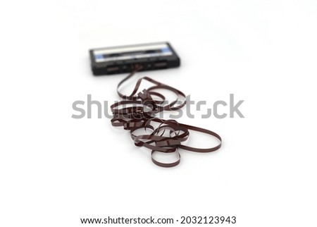This shows a well known problem with the old fashioned compact cassettes: the tape used to come out, making the cassette useless. Vintage compact cassette tape on white background. Royalty-Free Stock Photo #2032123943
